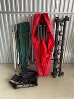 Overall view of three items including red tarp in bag, green bag with frame, and black mounting rails.