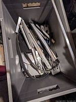 Plastic tote filled with numerous thin and thick flat metal strips and bars, some with notches and irregular shapes.