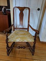 Front view of antique wooden rocking chair showing the carved backrest, armrests, and cushioned seat.