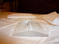 Close-up side view of a single clear glass prism with curved top surface placed on white protective paper.