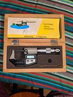 Electronic digital outside micrometer with digital readout inside wooden box with operating instructions on lid.