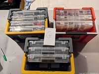 Three large plastic organizers with clear compartment boxes labeled and filled with hardware items.