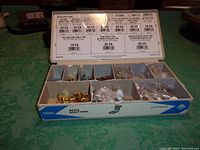 Top view of open Hillman metal shelf pins case showing various pins in compartments, with product info label inside lid.