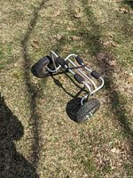 Metal framed kayak wheel set with two large inflatable rubber tires on grassy ground showing foam padding.