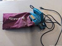 Full view of Makita power planer with maroon dust collection bag attached.