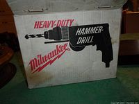 Cardboard box labeled Milwaukee Heavy-Duty Hammer Drill with graphic of drill on front.