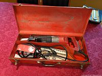 Milwaukee Sawzall in open metal carrying case showing saw and cord inside with instruction manual underneath