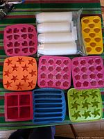 Rubber ice cube trays in various shapes and colors alongside sealed packs of mini plastic cups