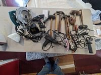 Overview of the tools spread on a pale table including circular saw, hammers, drills, and other hand tools.