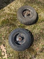 Two cart wheels on grassy ground showing tires, metal hubs, and included nuts/ washers.