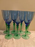 Front view of seven vintage Crate & Barrel wine glasses with blue bowls and green stems and bases, arranged in a row.