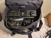 Overhead view inside backpack showing original Xbox console, controllers, cables packed inside