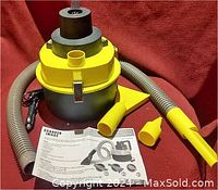 Photo showing Sharper Image branded wet/dry car vacuum with yellow and gray body, attached hoses and nozzles, instruction manual laid out.