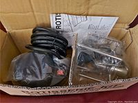 Motorized rotisserie parts in original box including wrapped motor with cord, metal spits and forks, and instruction sheet.