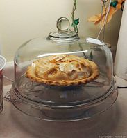 Pie placed on glass serving platter covered by clear dome cover with knob handle photographed to show dome in use and size.