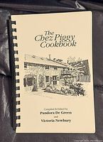 Cover page of 'The Chez Piggy Cookbook' showing its title and illustration of a building, compiled and edited by Pandora De Green and Victoria Newbury.