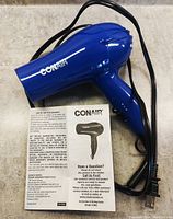 Conair blue hair dryer with attached cord, instruction manual placed nearby, showing product details and branding.