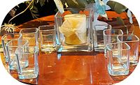 Wide view showing one central square crystal candle holder with white candle inside, surrounded by nine square shot glasses arranged in circle.