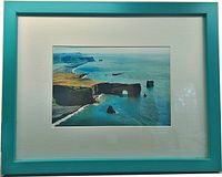 Framed print with teal wooden frame and white matting showing coastal scene with cliffs and ocean.