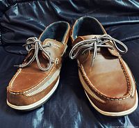 Front view showing moc-toe brown leather shoes with side inset ventilation panels, white contrast stitching, and lace-up closure with striped laces.