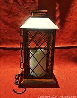 Front view of the rectangular outdoor metal lantern with crisscross glass panels and candle inside.