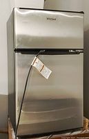 Exterior view of stainless steel Whirlpool bar fridge showing front with attached power cord and Whirlpool logo.
