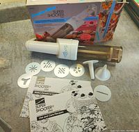 Proctor-Silex Super Shooter cordless cookie press device with six metal shaping discs, two plastic nozzles, original instruction manuals, and original box.
