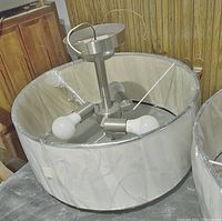 View of the inside of the three light drum pendant fixture showing three light sockets on a central metal rod inside the drum shade wrapped in protective plastic.