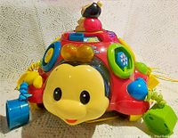 Front view of ladybug toy showing smiling bug face, shape sorter slots on sides, and various colorful buttons.