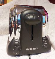Front view of the West Bend toaster showing control knobs for cancel, color settings, reheat and frozen buttons and the logo.