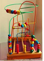 Front side view of large bead maze puzzle showing curved metal wires and beads on natural wood base