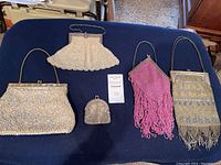 All five purses laid out on dark blue surface showing variety of sizes, beading styles, metal frames and some fringe