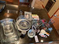 Photo showing clear Pyrex glass baking pans, measuring cups, glass mixing bowls, white ceramic plate, and some plastic measuring spoons and kitchen utensils on countertop.