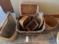 Group photo of seven assorted baskets on tiled floor in front of wall, showing variety in size, shape, material, and colors.