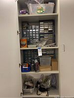 Wide shot of white storage cabinet with multiple shelves filled with blue and clear plastic organizers containing various fasteners.