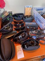 Wide view showing numerous sunglasses with their cases arranged on a wooden surface.