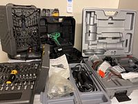 Multiple tool kits in plastic carrying cases including Hitachi drill set with bits, Dremel rotary tool, and a heat gun without case.