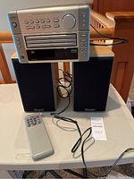 Denon UD-M5 CD auto changer receiver sitting on top of two Mission bookshelf speakers. Remote control placed in front on the table.