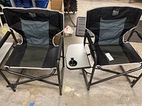 Photo showing two Timber Ridge folding camping chairs with black and gray fabric, metal frames, padded armrests, and attached side tables with cup holders.