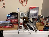 View of the full collection showing multiple boxed and loose grilling accessories, electronic motor, meat tenderizer, and grilling tools on a white surface.