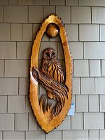 Front view of oval wood carving featuring detailed owl figure against gray shingle siding.