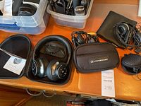 Wireless Sennheiser over-ear headphones in hard clamshell case with attached instructions on wooden table alongside a Sennheiser branded soft case.