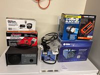 Photo showing all devices including battery tester, power converter, ozone generator, air treatment system, and battery charger on white surface.