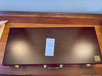 Closed view of dark polished wooden case for Mahjong set with golden emblem.