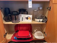 Kitchen cabinet shelf showing Ninja blender with user manual, Krups egg cooker, Pyrex dishes with carriers, and microwave cooking accessories.