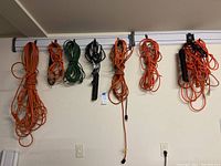 Wide shot showing multiple extension cords in orange, green, and black hanging from wall-mounted hooks.