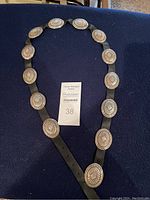 Full length view of black leather concho belt with all 13 silver conchos and buckle laid out