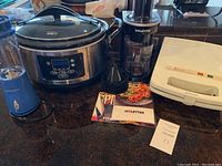Photo of Hamilton Beach slow cooker, Gourmia spiralizer with cones and manual, small Hamilton Beach blender, placed on countertop.