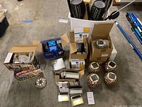 Lot overview showing various boxed solar garden lights, mosaic solar lanterns, and LED solar lights on concrete floor