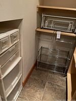 Metal storage rack on floor with wire shelves and plastic coated white shelf extension on wooden shelf above, plastic drawers stacked on side